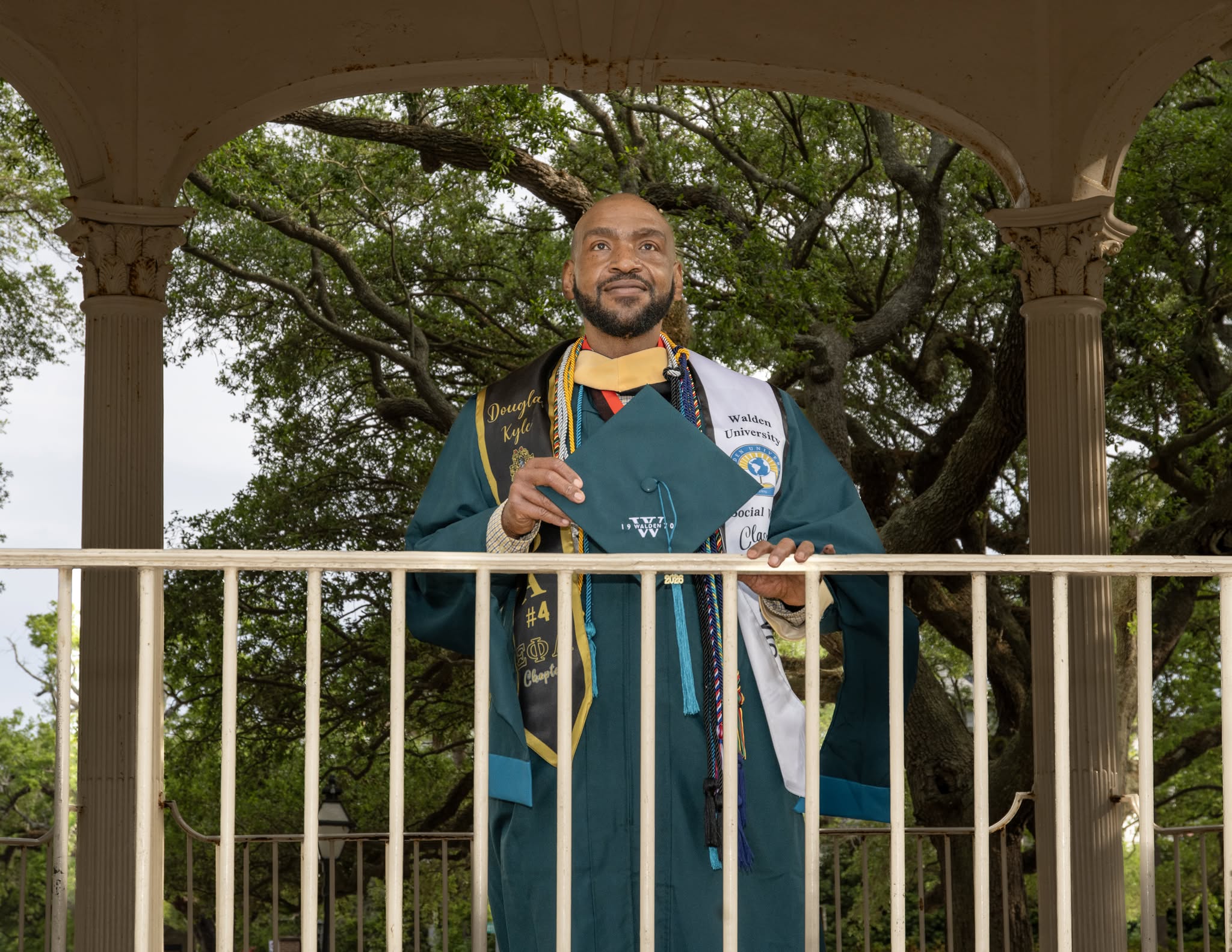 Walden University graduate holding his cap while posing in a gazebo