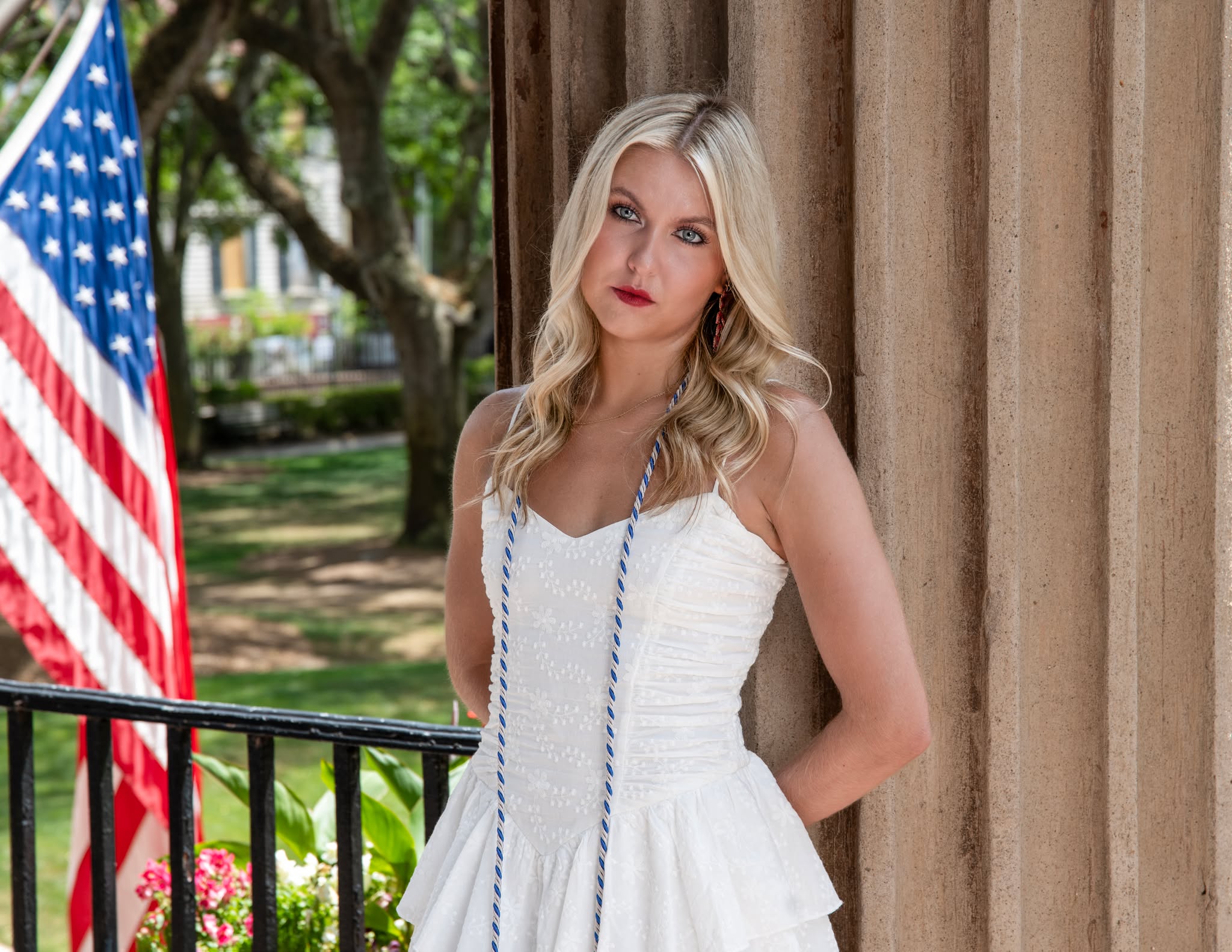 College of Charleston senior in a white dress posing beside an American flag