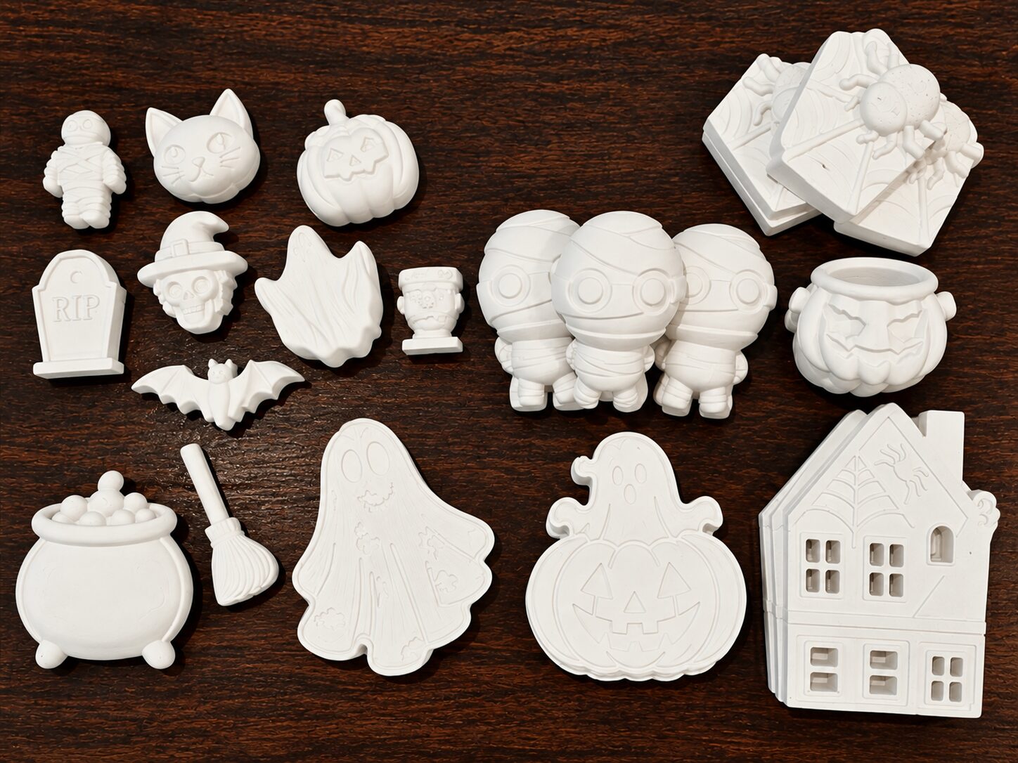 Assortment of white Halloween paint kit pieces from The Palmetto Pineapple, including ghosts, pumpkins, mummies, a cauldron, and a haunted house